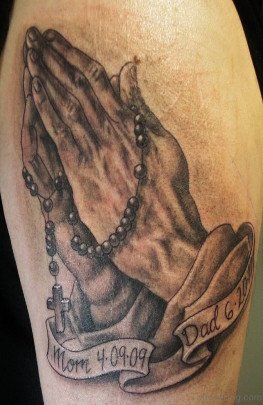 Black And Grey 3D Rosary Cross In Praying Hands With Banner Tattoo On Shoulder